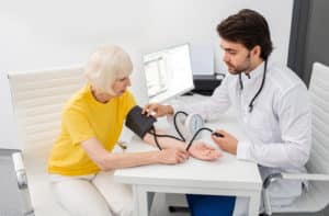 Doctor in clinic measures body pressure of an senior woman.